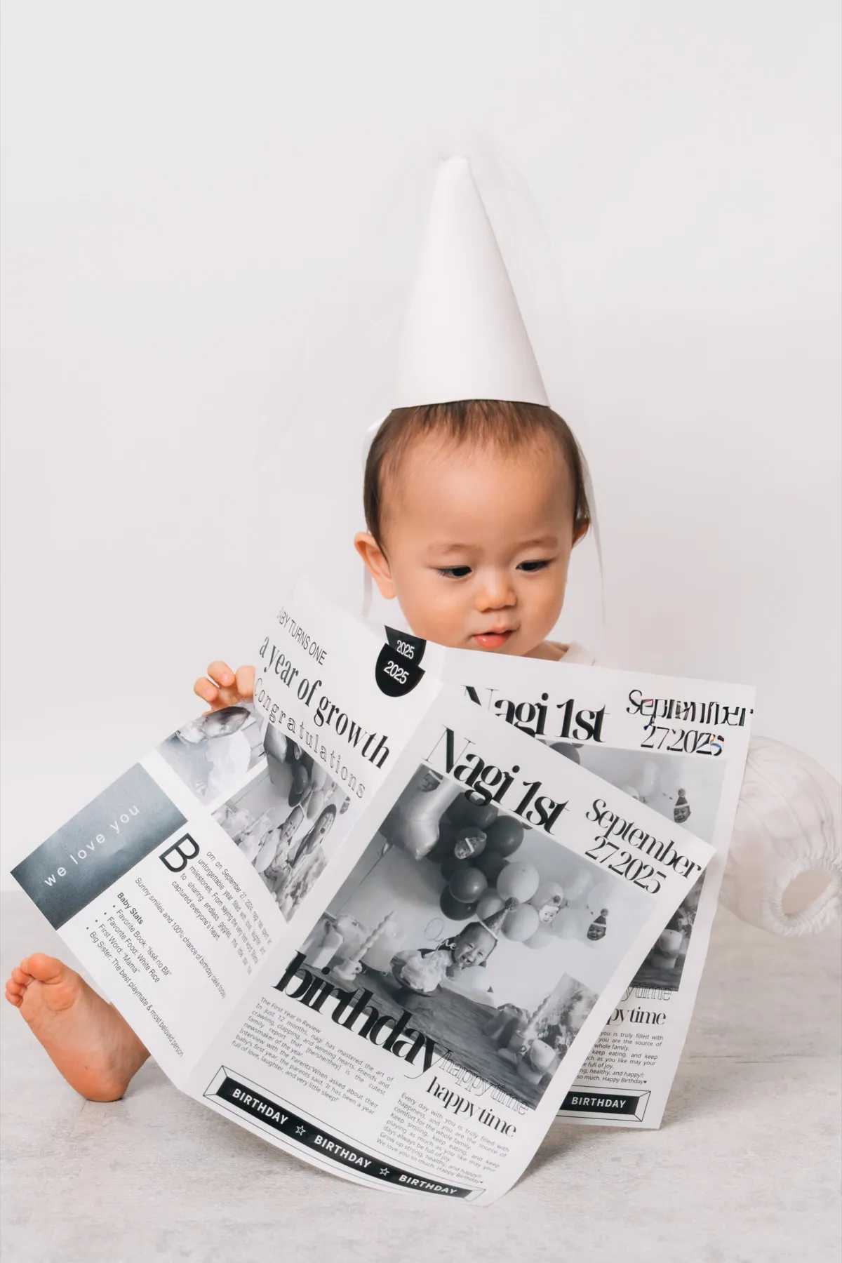 新聞紙の帽子をかぶって、手作りの誕生日新聞を広げて見る1歳の赤ちゃん